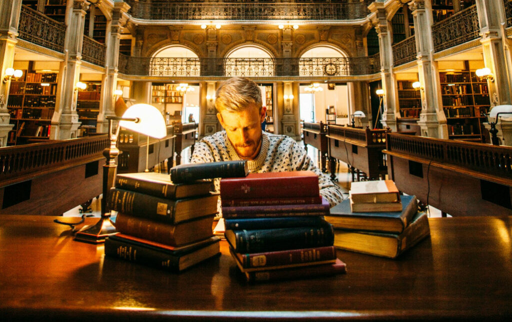 Junger Mann in Blibliothek hinter Büchern am Lernen