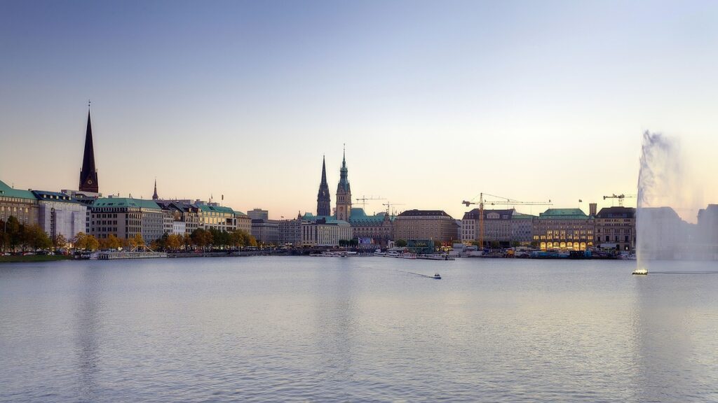 Die 4 besten Sportaktivitäten in Hamburg. Die Alster ist zu sehen und die Hamburger Innenstadt im Hintergrund. Die Abendsonne fällt auf das Wasser.