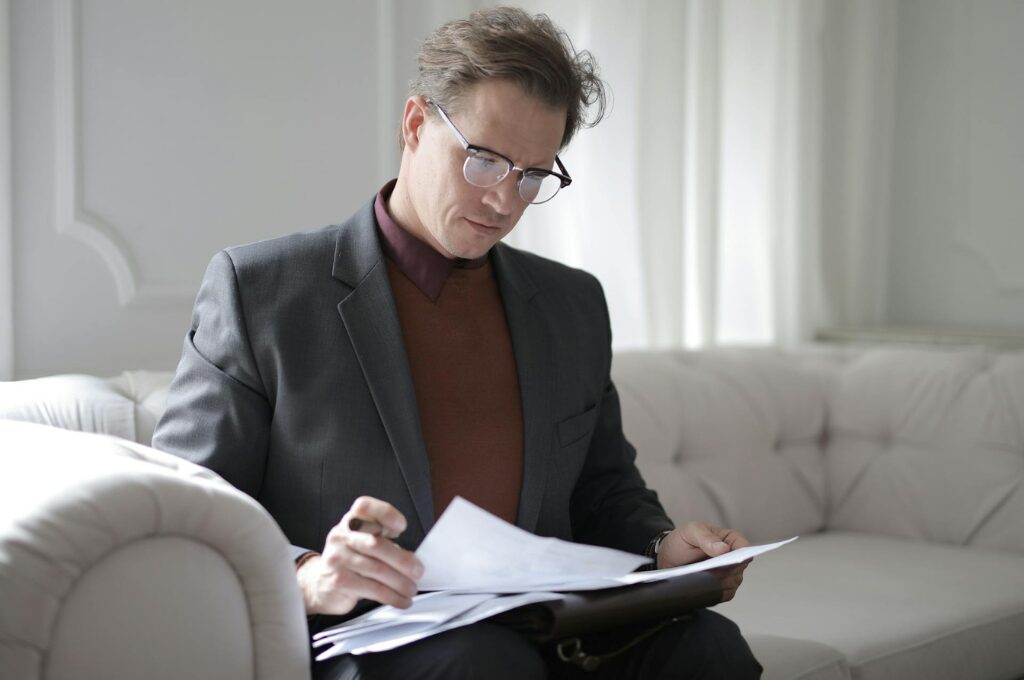 Schufa-Score: Ein Mann sitzt auf der Couch und schaut seine Dokumente an