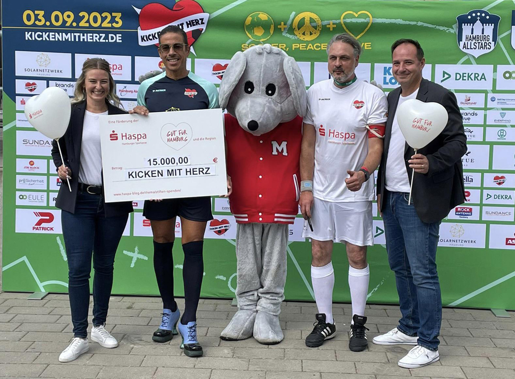 Großer Scheck für den guten Zweck (von links): Henriette Huth (Haspa), Jorge Gonzales auf High-Heels-Fußballschuhen (Promi-Auswahl "Hamburg Allstars"), Prof. Dr. Thomas Mir (Initiator und Kapitän der Ärzte-Mannschaft "Placebo Kickers") und Dennis Bade (Haspa)