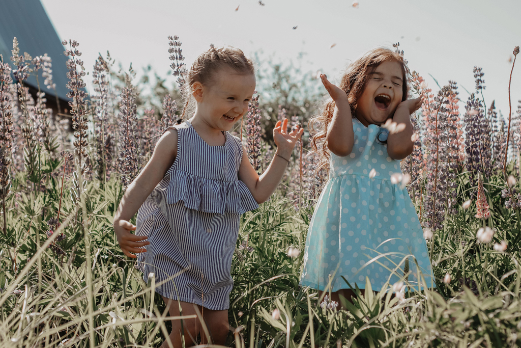 weltkindertag: zwei fröhliche kleine Mädchen spielen auf einer Wiese mit hohem Gras und Blumen