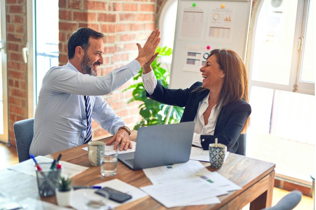 Arbeitszeit reduzieren: Ein Mann und eine Frau klatschen sich am Schreibtisch sitzend ab