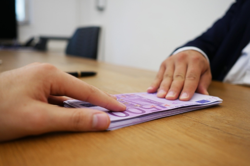 Geld abheben bei der Sparkasse: Hand schiebt einen Stapel 500 Euro Scheine über Tisch zu einer anderen Hand