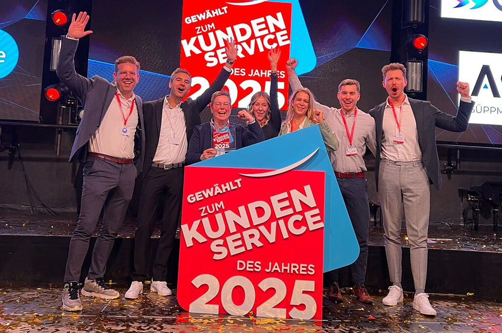 Drei frauen und vier Männer stehen auf einer Bühne mit Konfetti hinter einem großen Schild mit der Aufschrift "Gewählt zum Kundenservice des Jahres 2025"