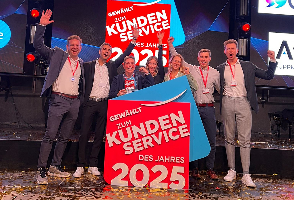 Drei frauen und vier Männer stehen auf einer Bühne mit Konfetti hinter einem großen Schild mit der Aufschrift "Gewählt zum Kundenservice des Jahres 2025"