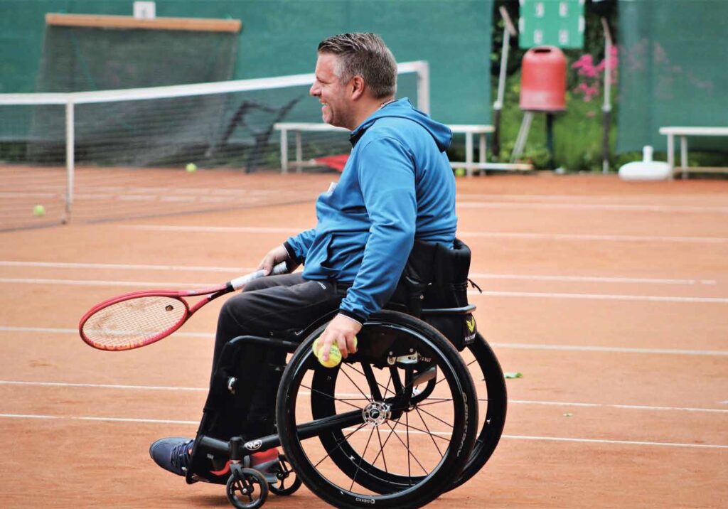 Mann im Rollstuhl mit Tennisschläger auf Tennisplatz